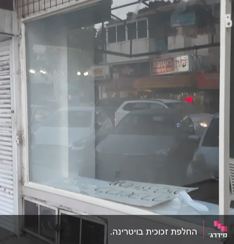 חלון זכוכית גדול עם השתקפות מכוניות וחנויות